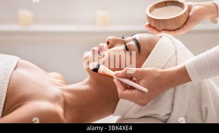 Thérapeute de beauté appliquant un masque facial sur la peau des jeunes femmes asiatiques au spa Banque D'Images