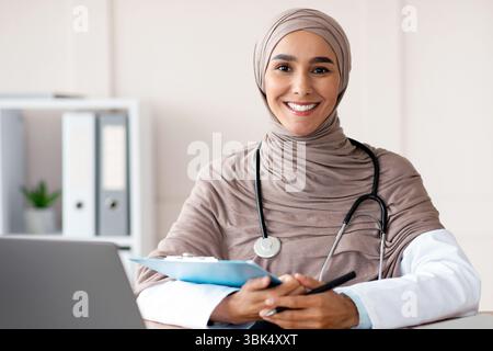 Jeune femme souriante médecin en hijab prenant anamnèse en clinique Banque D'Images