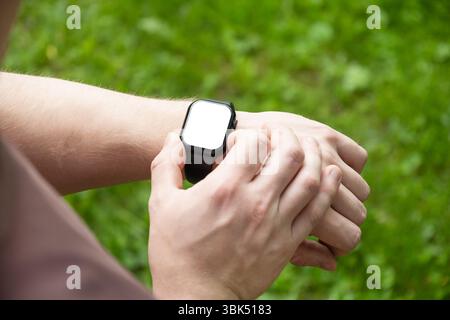 Gros plan des mains de l'homme vérifiant les applications avec smartwatch à fond vert nature. Pouls de contrôle masculin, battement de coeur et autres. Tracker de fitness. À l'extérieur. Banque D'Images