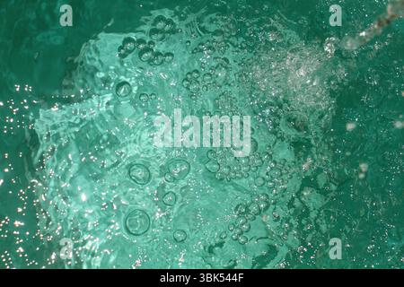 Un moment dynamique d'eau bouillonnant vigoureusement sous la lumière directe du soleil. L'eau apparaît turquoise et claire, avec de nombreuses bulles d'air. Banque D'Images