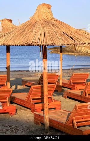 Chaises longues en bois et parasols en paille, Tinos, le groupe d'îles des Cyclades, Grèce. Prise juin 2025 été Banque D'Images