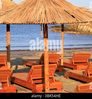 Chaises longues en bois et parasols en paille, Tinos, le groupe d'îles des Cyclades, Grèce. Prise juin 2025 été Banque D'Images
