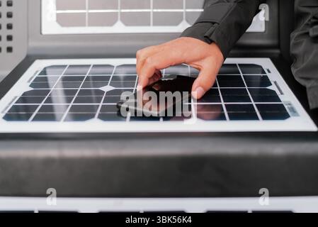 Une main pose délicatement un smartphone sur un panneau solaire brillant, symbolisant la connexion intelligente entre énergie propre et technologie moderne. Un pas vers Banque D'Images