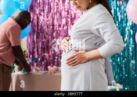 Femme asiatique enceinte debout dans le profil tenant le ventre pendant la partie de révélation de sexe tandis que Black Man en arrière-plan Banque D'Images