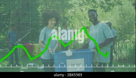 Bénévoles portant des T-shirts bleus tenant le bac à dons et triant dans le parc, avec des boîtes de table de pique-nique Banque D'Images