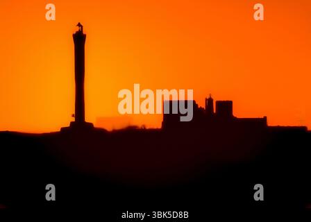 Maintenant plus sombre que le soleil : la silhouette noire floue d'une centrale nucléaire désaffectée contraste avec un coucher de soleil orange profond sur Dungeness, Kent, Angleterre, Royaume-Uni. L'œuvre d'art numérique de la capture d'image de 2006 comprend le phare de 1904 qui a utilisé une lampe à paraffine plus un successeur des années 1960 s'élevant à 43 m ou 141 pieds au-dessus du cap Dungeness en bardeaux qui avance dans le détroit de Douvres, dans la Manche. Banque D'Images