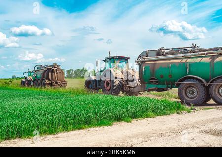 Deux tracteurs agricoles avec des remorques contenant des réservoirs avec des engrais organiques, fumier. Les tracteurs roulent sur la route parmi les champs verts. Vue latérale Banque D'Images