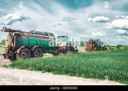 Deux tracteurs agricoles avec des remorques contenant des réservoirs avec des engrais organiques, fumier. Les tracteurs roulent sur la route parmi les champs verts. Vue latérale Banque D'Images