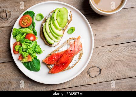 Pain grillé à l'avocat et au saumon avec fromage à la crème et légumes, vue de dessus. Petit déjeuner sain sandwichs ouverts avec saumon et avocat sur fond de bois. Banque D'Images