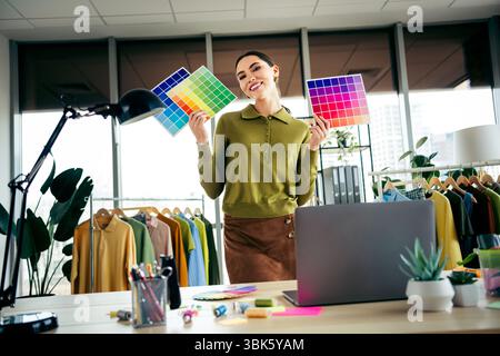 Jeune entrepreneur de mode tenant des palettes de couleurs dans un bureau d'atelier élégant mettant en valeur la créativité du design et les textiles Banque D'Images