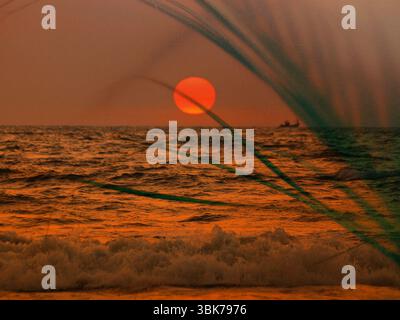 Un coucher de soleil ou un lever de soleil à couper le souffle avec une mer calme et un grand soleil rouge se couchant à l'horizon. Une atmosphère tranquille sur une côte tropicale, rivage. Le silho Banque D'Images