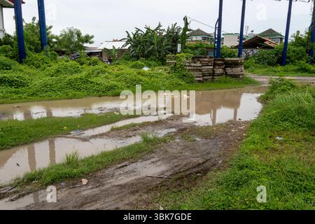 Route boueuse avec beaucoup de mauvaises herbes et de déchets. La route est inondée et l'eau est trouble Banque D'Images