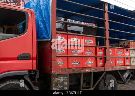 Camion rouge avec une bâche bleue sur le dessus. Le camion est un camion transportant de la bière Bintang et garé sur une route de briques Banque D'Images