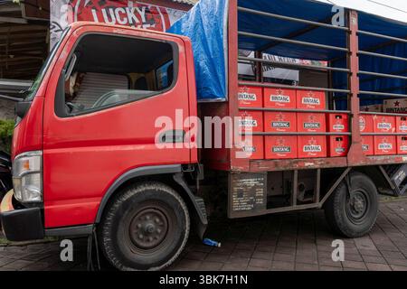 Camion rouge avec une bâche bleue sur le dessus. Le camion est un camion transportant de la bière Bintang et garé sur une route de briques Banque D'Images