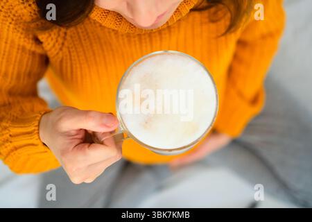 Gros plan aérien d'une femme enceinte profitant d'un latte dans une pose de méditation, réfléchissant sur les directives diététiques. Atmosphère chaleureuse de plaisir conscient. Banque D'Images