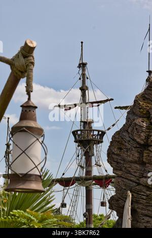 Une vue d'un mât de bateau pirate avec une lanterne au premier plan contre un ciel partiellement nuageux à Disneyland Paris, France. Banque D'Images