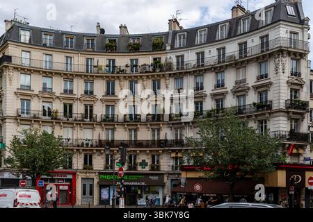 Cet édifice incurvé de plusieurs étages à Paris présente des détails architecturaux ornés, des balcons ornés de plantes et des vitrines au rez-de-chaussée. Banque D'Images