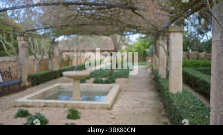 Jardin floue avec un style méditerranéen, fontaine défocalisée et chemin sous lumière bokeh, créant une atmosphère sereine avec une végétation luxuriante Banque D'Images
