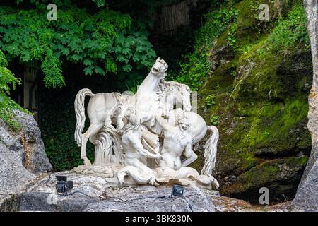 Sculpture en marbre de personnages et de chevaux dans une scène dynamique, entourée de verdure luxuriante et de terrain rocheux. Projecteurs ci-dessous aux jardins de Versailles, pari Banque D'Images