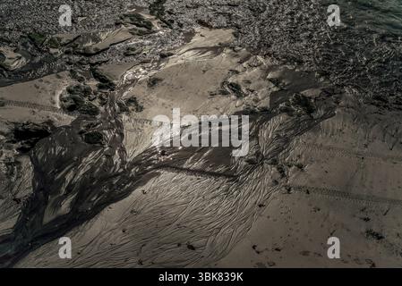 Motifs de vagues, pieds d'oiseau, empreintes humaines et traces de pneus dans le sable sur le point d'être lissé par la marée entrante à Mullion Cove sur la péninsule de Lizard et Lizard Heritage Coast, Cornwall, Angleterre, Royaume-Uni. Illustration numérique à partir d'une image capturée en octobre 2013. Banque D'Images
