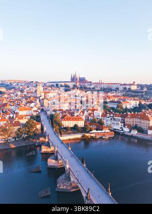 Une vue aérienne à couper le souffle capture la ville médiévale de Prague au lever du soleil. La lumière chaude met en valeur le pont Charles, la rivière Vltava et l'architecture historique, créant une atmosphère sereine le matin. Banque D'Images