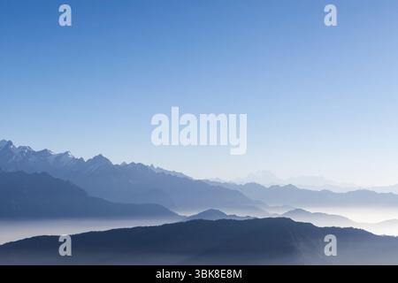 Fond de chaîne de montagnes brumeuse avec ciel bleu et brume blanche dans le soleil tôt le matin. Sommets enneigés des montagnes de l'Himalaya à l'horizon au Népal. Banque D'Images