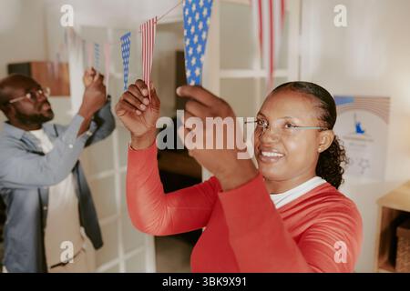 Femme afro-américaine accrochant des drapeaux américains avec un homme d'âge moyen souriant Banque D'Images