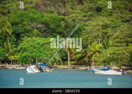 Un bateau abandonné repose près de la rive de Sapzurro, Choco, entouré d'une végétation luxuriante et d'eaux calmes. Banque D'Images