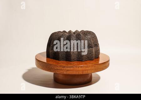 Un gâteau de bundt de riz gluant noir entier placé sur un support de gâteau rond en bois sur un fond neutre. Concept de dessert asiatique traditionnel. Banque D'Images
