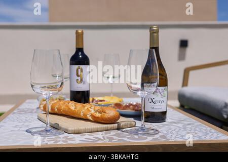 Gros plan d'une table en plein air avec du vin, des verres, du pain et des collations préparés pour un repas relaxant sous le soleil. Banque D'Images