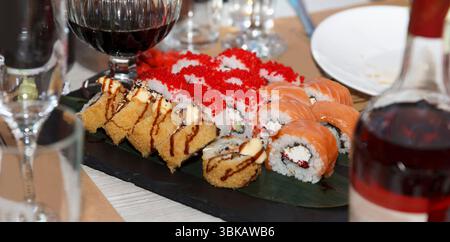 Une variété de rouleaux de sushi, y compris frits, saumon, et recouverts de roches servis sur une assiette d'ardoise avec du vin rouge sur une table intérieure festive Banque D'Images