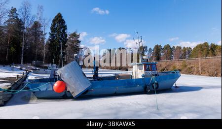 De petits chalutiers de pêche continentale ancrés et coincés dans la glace au printemps à la marina de Kivisalmi, lac Etelä-Konnevesi, Finlande Banque D'Images