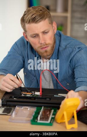 homme testant un ordinateur portable cassé avec un multimètre Banque D'Images