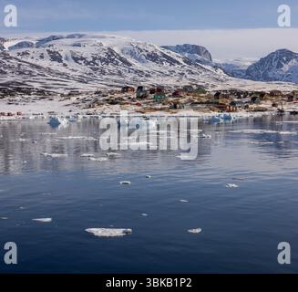 Vue sur la colonie groenlandaise éloignée de Saqqaq avec la glace de mer dispersée au printemps, les maisons colorées et les montagnes enneigées dans l'ouest du Groenland. Banque D'Images
