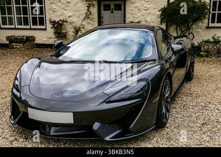 Élégante voiture de sport noire de luxe McLaren des années 570 garée sur une allée de gravier devant une maison de campagne anglaise traditionnelle Banque D'Images