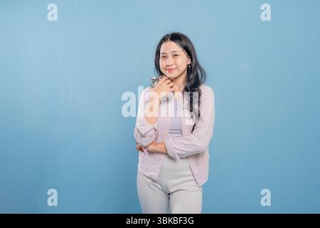 Une femme est debout devant un mur bleu, regardant vers le bas et pensant. Elle porte une chemise blanche et un pantalon blanc Banque D'Images