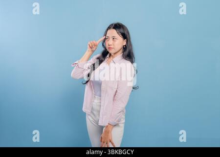Une femme se tient debout devant un mur bleu, portant une veste rose et un pantalon blanc. Elle regarde en bas et elle est profondément dans la pensée Banque D'Images