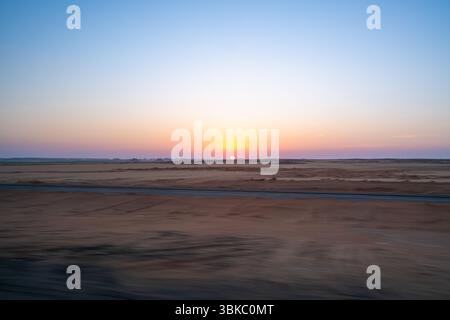 Un lever de soleil à couper le souffle peignant le vaste désert d'Assouan en Egypte, vu d'un véhicule en mouvement sur la route menant aux anciens temples d'Abu Simbel, avec Banque D'Images