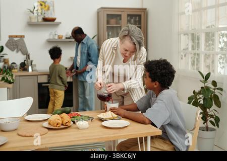 Famille appréciant le repas ensemble dans la cuisine remplie de lumière avec enfants et adultes préparant la nourriture, table de mise créant une atmosphère chaleureuse et accueillante Banque D'Images