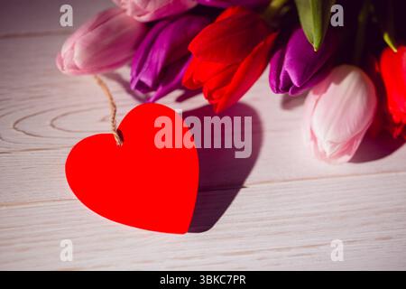 Conception plate montrant l'étiquette rouge en forme de coeur nouée par ficelle sur le dessus de table blanchi à la chaux avec des tulipes colorées Banque D'Images