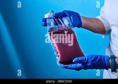 Scientifique porter des gants bleus main tenant la poche de sang rouge du donneur au laboratoire de banque de sang.médecin et sang frais pour transfusion.Save vie con médical Banque D'Images