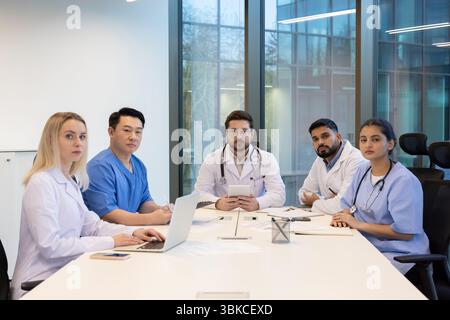Un groupe diversifié de professionnels de la santé assis à une table dans un bureau moderne, engagé dans une réunion. Banque D'Images