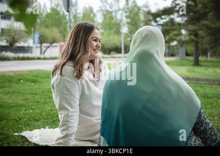 Deux femmes de différentes ethnies parlant sur une couverture de pique-nique dans le parc Banque D'Images