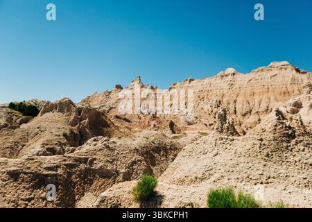 Crêtes et pentes rocheuses ensoleillées sous un ciel bleu vif dans les Badlands Banque D'Images