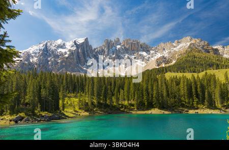 Les eaux turquoises époustouflantes du lac Carezza avec une dense forêt de pins au premier plan, et le majestueux groupe de Rosengarten enneigé dominant th Banque D'Images