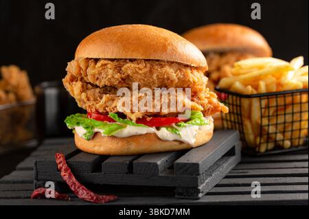 Hamburger de poulet croustillant servi avec des frites sur fond noir. Banque D'Images