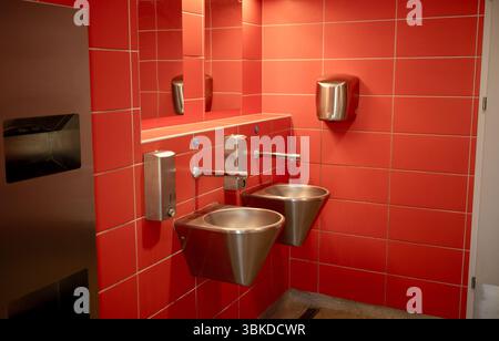Toilettes publiques modernes avec murs carrelés rouges et lavabos en acier inoxydable Banque D'Images