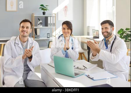Heureux souriant médecins applaudissant à une réunion assis au bureau sur le lieu de travail dans la clinique. Banque D'Images