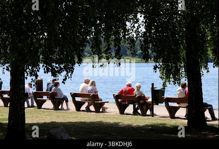 20 juin 2025, Mecklembourg-Poméranie occidentale, Waren (Müritz) : vacanciers et touristes assis sur des bancs sur les rives du Müritz par temps estival. Le temps ensoleillé domine la région des lacs de Mecklenburg. Photo : Bernd Wüstneck/dpa Banque D'Images