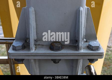 Gousset soudé et bride boulonnée sur colonne en acier gris contre poutres de support jaunes Banque D'Images